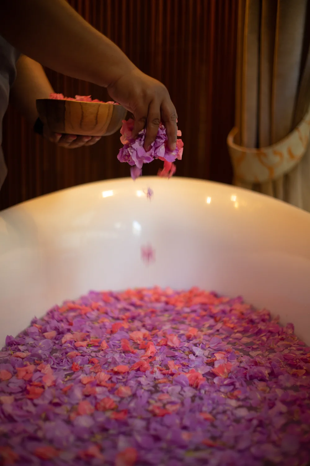 Pink and violet petals scattered into a candlelit bath