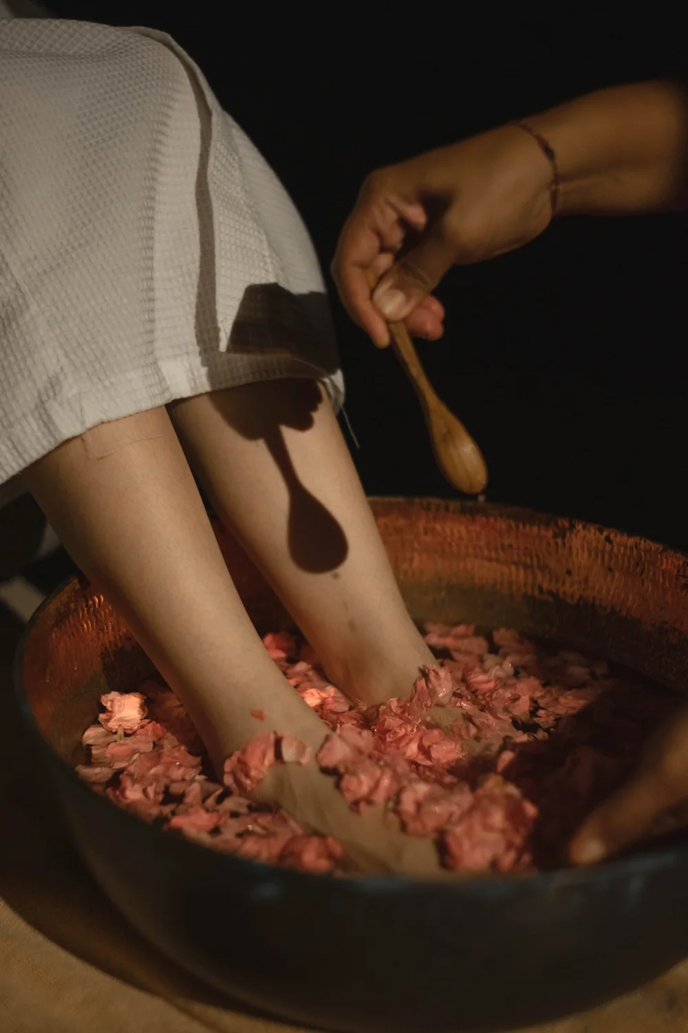 Feet resting in a copper bowl of warm water and rose petals while salt is spooned in
